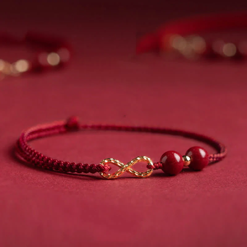 Braccialetto alla cavigliera con simbolo dell'infinito dorato e cordino rosso con Buddha Stones e cinabro.